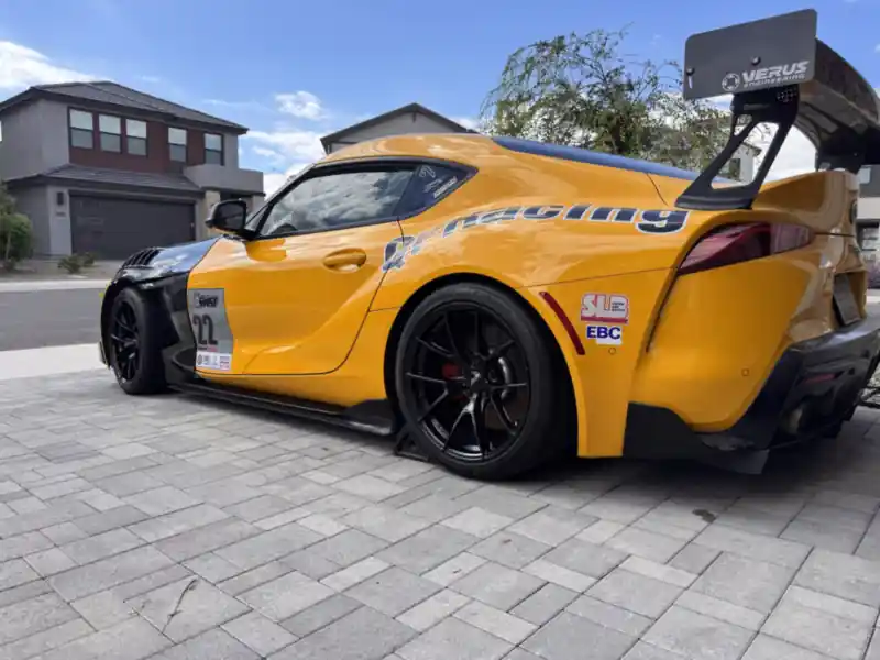 Yellow Toyota GR Supra race car with a carbon fiber wing, freshly detailed in a driveway